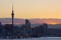 The Sky Tower and other tall buildings create the skyline of Auckland City, New Zealand where views from across the harbour allow people to admire this and the sunset.