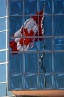 A large Canadian flag flies in the breeze and can been seen reflected in the windows of a building at Sackville Landing in Halifax Harbour, Nova Scotia. The Canadian flag is a symbol of Canadian pride and patriotism.