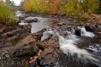 A small waterfall flows over the rocks as colorful Autumn leaves swirl about in the Restoule River in the town of Restoule in Ontario, Canada.