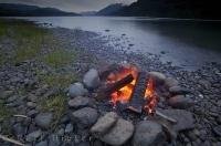A campfire burns as dusk sets around the tranquil aura of Nimpkish Lake on Northern Vancouver Island in British Columbia, Canada.