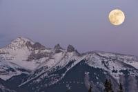 A winter scene of the snow covered Fairholme Range in the Banff National Park has a large full moon as its backdrop. Banff National Park is part of the Canadian Rocky Mountains.