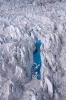 An aerial view of a brilliant blue lake caught between the crevasses of Fox Glacier in Westland National Park situated on the West Coast of the South Island of New Zealand.