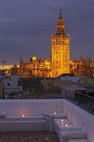 La Giralda tower attached to the Seville Cathedral is lit up at dusk, and can be seen in full view from the balcony of the Banos Arabes, the Arab Baths. The Cathedral is located in the Santa Cruz district in Sevilla, Andalusia, Spain.