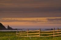 Jagged off shore islands buffer the coastal waters of the Atlantic Ocean while a rustic fence adds to the dynamics of the beautiful scenery during sunset on the west coast of Newfoundland, Canada.