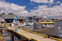 Fishing boats tied to the brightly painted sides of the wharf in the harbour of the small town of North Rustico in Queens, PEI.