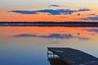 The bright orange colours of sunset lingering in on the horizon as the light fades at dusk over Lake Audy, Riding Mountain National Park, Manitoba, Canada.