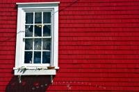 A window with a light shining inside stands out against the red wall of the Lunenburg Outfitting Co building situated in the town of Lunenburg in Nova Scotia, Canada. The small town of Lunenburg is a UNESCO World Heritage Site.