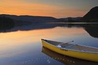 A canoe rests along the shores of Lake Monroe in Quebec, Canada where you can look over the hillsides and watch a beautiful sunset come to life.