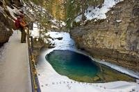 This beautiful scenic canyon is Johnston Canyon in Banff National Park in the Canadian Rocky Mountains. This pool, which is surrounded by ice and snow is a popular tourist attraction in Alberta and many visitors make it a point to stop here.