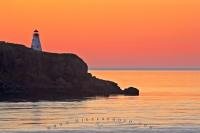 The sunset turns the sky to shades of pink and orange over the Boar's Head Lighthouse on Long Island, as seen from across Petite Passage between Digby Neck and Long Island in the Bay of Fundy from Highway 217 in Nova Scotia.