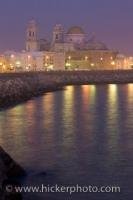 The waterfront lights stretch out across the waters of the Costa de la Luz at dusk while the grand Catedral Nueva, dominates the skyline in the city of Cadiz in the Andalucia region of Spain.