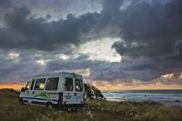 A brooding evening sky looms over a campervan at sunset. Camping along the Taranaki coastline at Cape Egmont is a fabulous experience with the waves crashing ashore just below the cliffs.