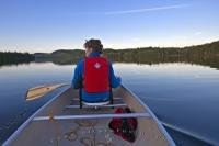 A woman enjoys an evening paddle in a canoe on Whitefish Lake in Algonquin Provincial Park, Ontario, Canada.