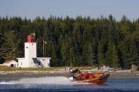 The Canadian Coast Guard backdropped by Pulteney Point Lighthouse in BC, Canada.