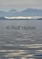 A crystal clear, smooth water of Johnstone Strait off Northern Vancouver Island with the British Columbia Coast Mountains in the background.