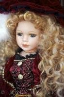 An elaborate and elegant porcelain doll features pretty long curly hair and victorian style clothing.
