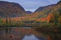 Jacques Cartier River in Quebec, Canada winds its way through the fall colored landscape as the lighting at sunset highlights the trees.