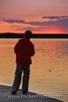 Silhouetted by a beautiful sunset over Lake Audy in Riding Mountain National Park, a young boy tries his hand at Northern Pike and Walleye fishing.