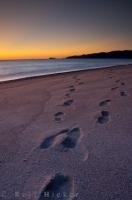 Footprints sink into the sand along the beach at Agawa Bay in Lake Superior Provincial Park in Ontario, Canada as the tones of colors reflect off the landscape at sunset.