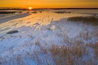 A beautiful close to an icy cold day as the sun settles on the horizon of a frozen lake at sunset  near the arctic community of Churchill, Manitoba.