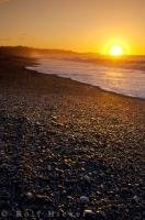 Standing on Gillespies Beach on the South Island of New Zealand, the sunset glistens off the rocks on the beach.