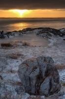 Clouds hover above the rocky coastline of the Hudson Bay in Churchill, Manitoba leaving a visible line across the sky where the sunset colors highlight the frozen area.