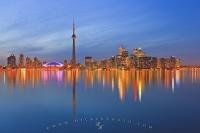 The illuminated Toronto skyline at twilight with colorful reflections on Lake Ontario.