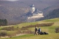 A twosome walks the Karlstein Golf Course in the Czech Republic while enjoying the scenery of the Karlstein Castle.