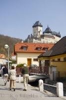 Tourists stroll through the village of Karlstein in the Czech Republic with the Karlstein Castle towering above them.