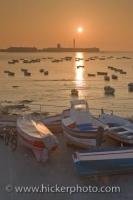 Fishing boats anchored in the water with some pulled ashore onto Playa de la Caleta in the City of Cadiz in Andalusia, Spain during the sunset hours.
