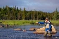 A man spends his day knee deep in the Salmon River near Main Brook, Newfoundland fly fishing amongst the wilderness under the sunny sky.