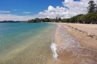 Waves lap up along the sandy beach in Mission Bay in Auckland on the North Island of New Zealand as the white billowy clouds move in across the horizon.