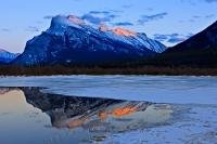 Mount Rundle appears cold and crisp during winter at dusk as it overshadows the partially frozen 2nd Vermillion Lake near the town of Banff in Alberta, Canada. This is in Banff National Park, which forms part of the Canadian Rocky Mountain Parks.