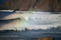 Sea spray trails a row of ocean waves topped with a beautiful rainbow along the Oregon Coast, USA.