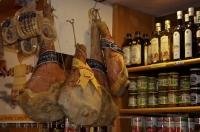 Delicious Prosciutto from Parma hanging beside shelves of bottles, jars and cans in a shop in Venice, Italy.