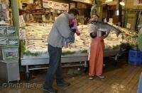 One of the famous fish throwers at the Pike Place Fish Co in downtown Seattle shows a child a large fresh salmon.