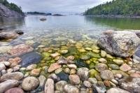 With fog hovering in the distance, the crystal clear and calm water of Lake Superior reveals the rocky shoreline of Sinclair Cove in Lake Superior Provincial Park of Ontario, Canada.