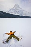 A tourist lies on her back and makes a snow angel after fresh snowfall on Waterfowl Lake during winter. The scenery in the background of this photo is Mount Chepren, located along Icefields Parkway in Banff National Park, Alberta.
