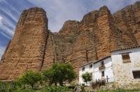 Towering walls of rock known as Los Mallos de Riglos, dwarf the white houses in the village of Riglos in Huesca, Aragon in Spain, Europe.