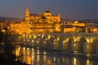 The Puente Romano spanning the Rio Guadalquivir in the province of Cordoba in Andalusia, Spain, is lit up at dusk with the Mezquita (Cathedral-Mosque) lit strikingly in the background. Cordoba is a popular tourist destination in Andalusia, Spain.