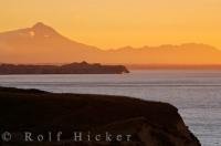 The scenery from the top of the cliffs at the northern end of the North Taranaki Bight in New Zealand is beautiful at sunset as a yellow glow highlights the volcano called Mt. Taranaki/Mt. Egmont.