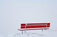 A white out sweeps through Andermatt, Switzerland and the only thing one can see is the bright red park bench.