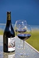 A bottle of red wine and two glasses stand on a glass-topped table on the terrace at Bonitas Winery in Summerland, British Columbia, Canada.