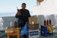 A wine vendor sitting in the shade of a treeing selling wine in Pyrgos Santorini Greece.